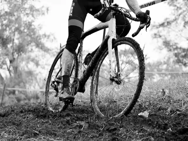 Veldrijfiets met modderige banden in een herfstig bos, onderkant van de renner in beeld
