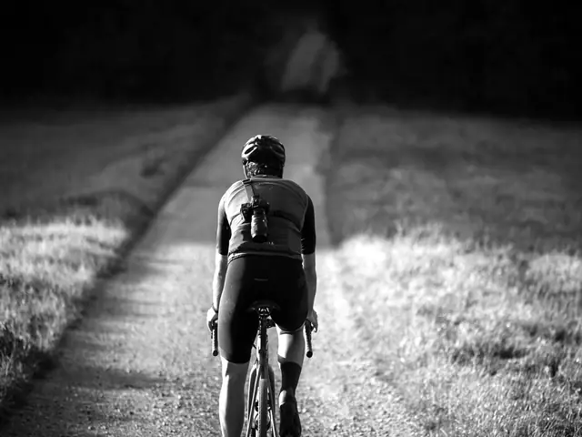 Wielrenner van achteren op een grindpad tussen grasranden in laag zonlicht