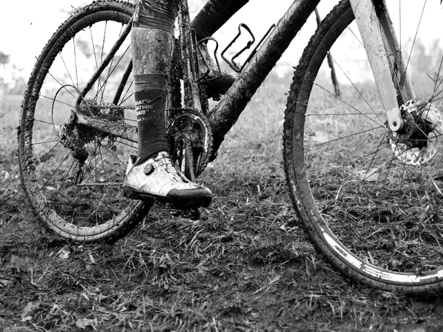 Detail van een modderige fiets en schoen op nat gras tijdens een veldrit
